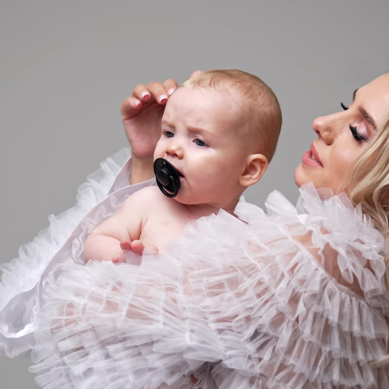 Kjærlig mor i hvit kjole vinker til sitt lille barn. Søt baby med smokk i munnen begynner å gråte. Hvit bakgrunn