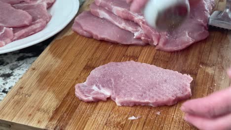 tenderizing pork with meat mallet tool - using meat pounder meat tenderizer to prepare slabs of pork and seasoning with salt for pork schnitzels recipe at home in kitchen