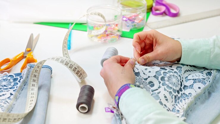 Seamstress hand sewing lace on denim fabric
