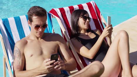Young-couple-using-phones-at-the-swimming-pool