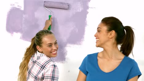 pretty girl painting wall with a brush smiles with another girl