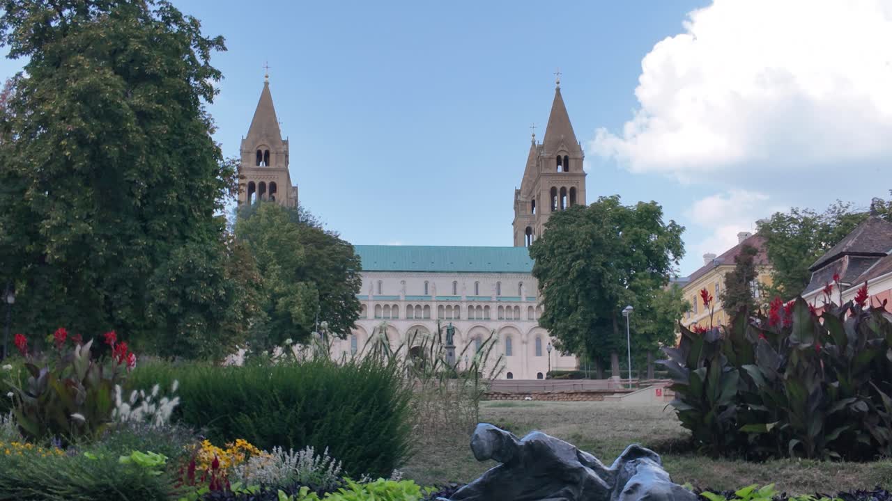 Pan from a vivid flower bed to Pécs Cathedral, highlighting the historic architecture and scenic urban charm