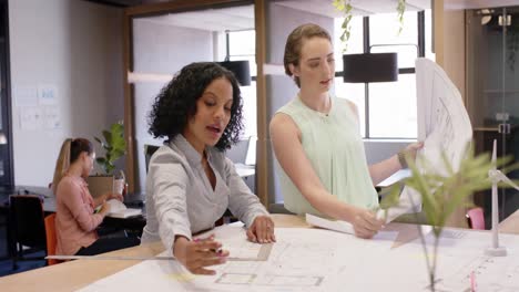 Diverse-female-architects-discussing-work-and-looking-at-blueprints-at-office,-in-slow-motion