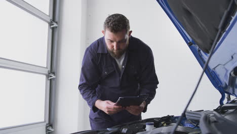 mecánico masculino en el garaje usando software de diagnóstico en una tableta digital para reparar el motor del coche