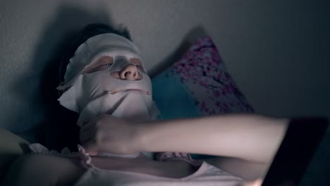 분홍색  ⁇ 을 입은 갈색 여성은 얼굴에 특별한 시트 마스크를 고정합니다.
