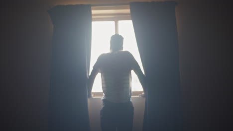 african american man opening the curtains in a dark room in the morning