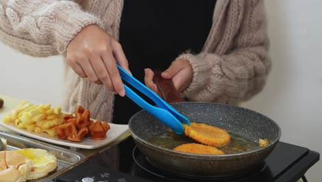 woman flipping chicken meat with bread crumbs on hot pan using tongs for cheeseburger