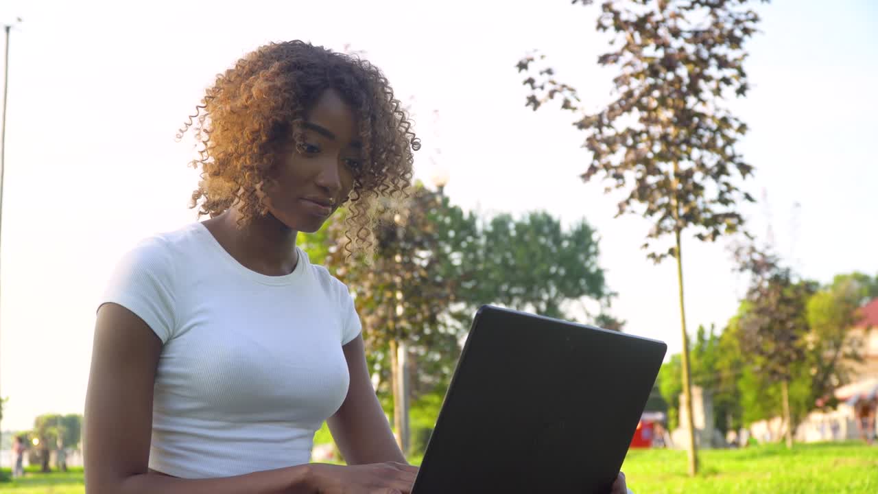 joven afroamericana usando una computadora portátil en el parque