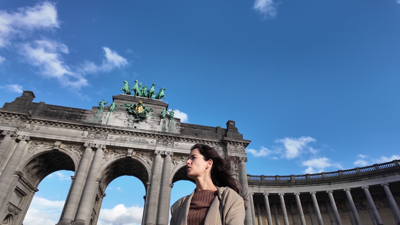 Confident woman standing before Cinquantenaire Arch under blue sky in Brussels