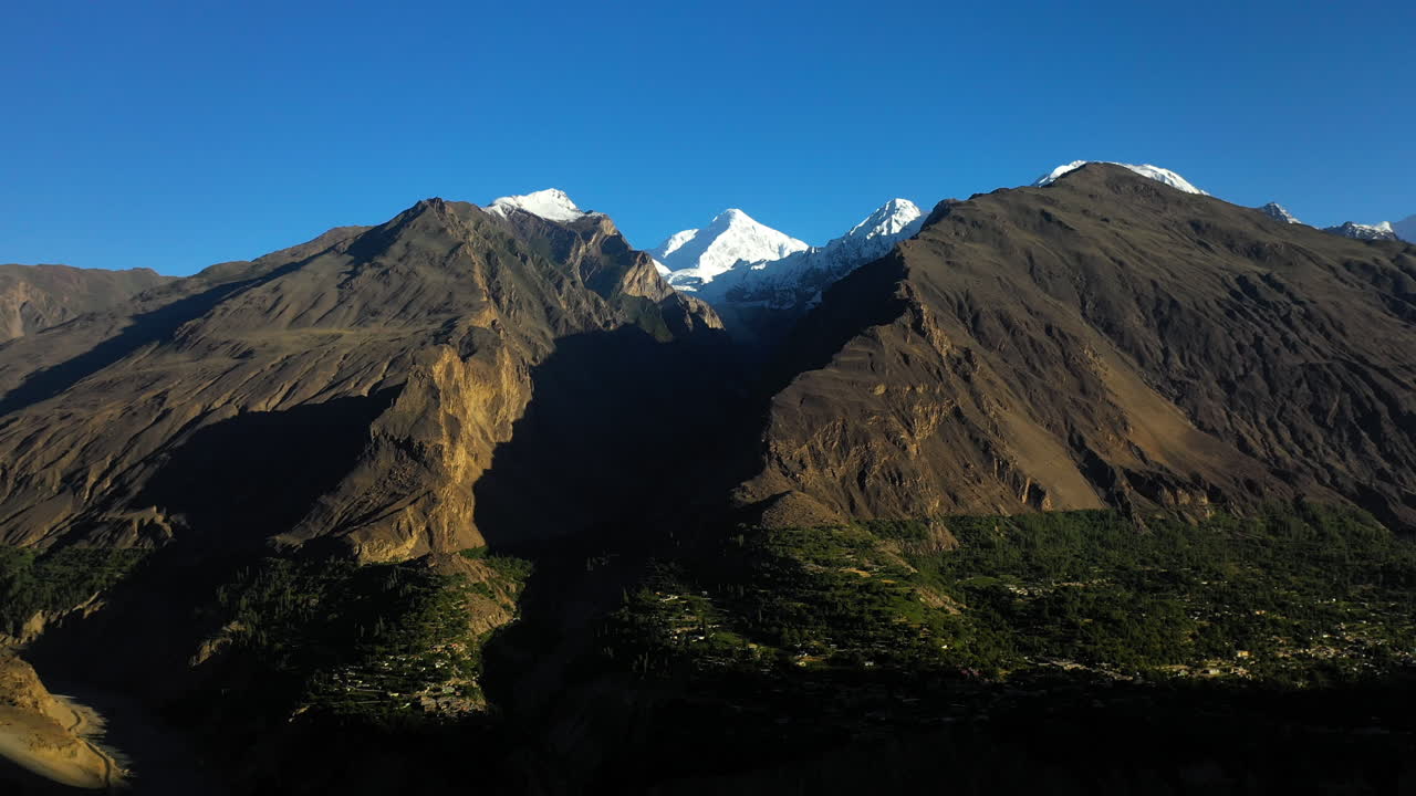 toma cinematográfica de drones del sol brillando en el valle, conos passu en hunza pakistán, picos montañosos cubiertos de nieve con acantilados empinados, toma aérea giratoria ancha