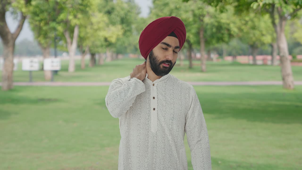 Uomo indiano Sikh malato che soffre di dolore al collo in un parco.