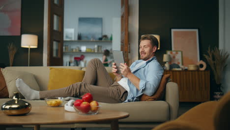 carefree gentleman laying tablet at evening home. positive guy watching computer