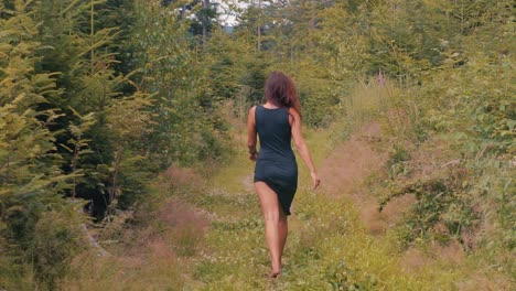 espalda de una mujer sexy con un vestido negro caminando descalzo sobre hierba verde en la naturaleza del bosque