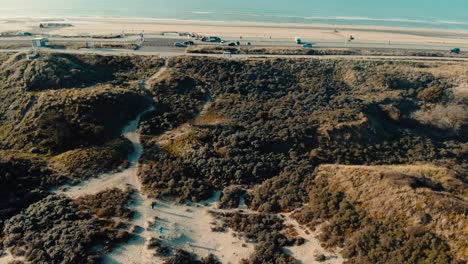 aerial birdseye above sandy dune terrain tilt up to coastal ocean road horizon