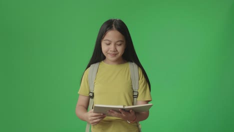 estudiante asiática con un libro en la mano y mirando mientras camina a la escuela en pantalla verde clave de croma