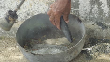 Close-up-hand-put-pieces-of-solid-lead-in-bar-to-melt-with-fire-lighter-to-bring-to-liquid