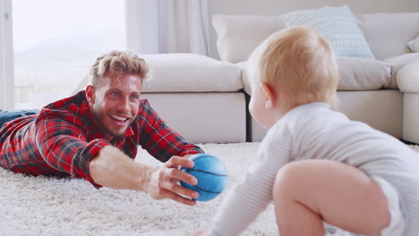 young father lying on floor playing with toddler son at home