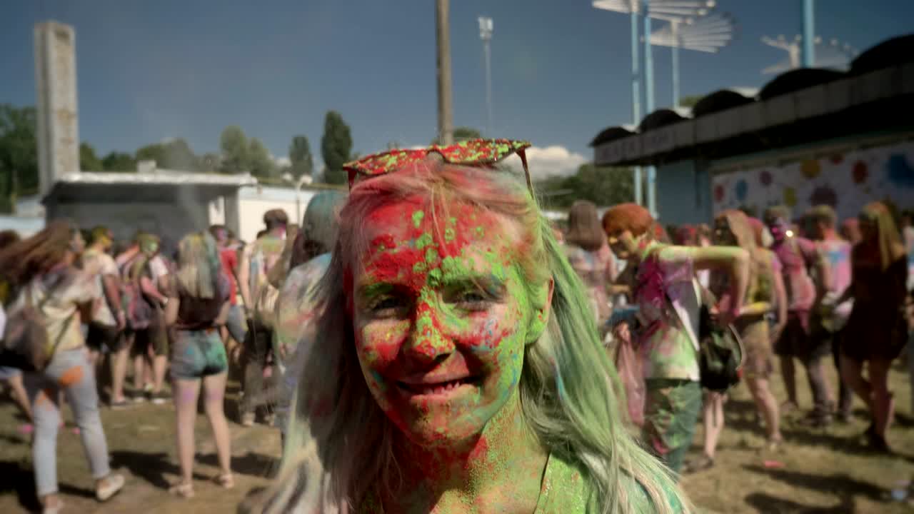 Giovane ragazza felice ricoperta di polvere colorata salta e scuote la testa al festival Holi di giorno in estate. Concetto di colore.