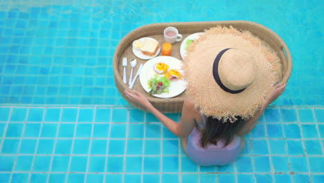 woman with sun hat on holiday taking breakfast by the pool