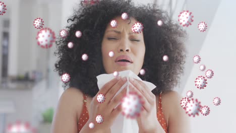 animation of coronavirus icons over mixed race woman sneezing at home