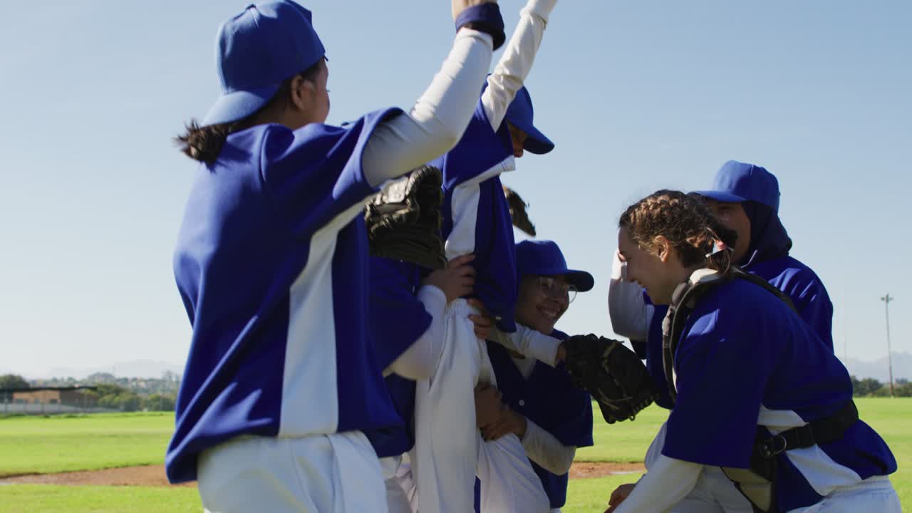 Squadra mista e felice di giocatrici di baseball che festeggiano dopo la partita, sollevando una compagna