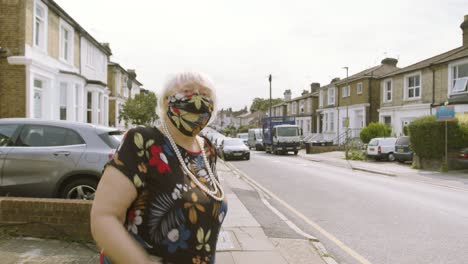 elderly woman wearing a face mask with matching dress walking onto the street looking around and waving