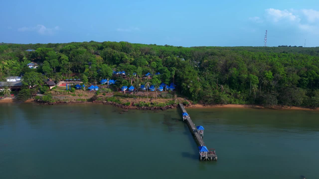 Koh Mak tropical island in Thailand showing luxury glamping tents on the coast near the pier surrounded by lush vegetation. Wonderful aerial view flight fly push forward drone