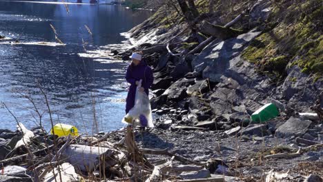 woman picking up plastic garbage from small rocky beach in norway