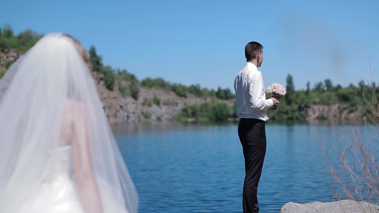 Bride And Groom By The River. Happy stylish bride and groom walking on the river, smiling and kissing