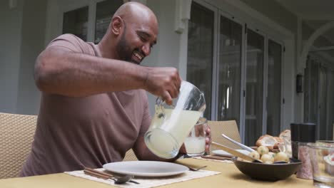 happy biracial parents and son serving meal at dinner table in garden, slow motion
