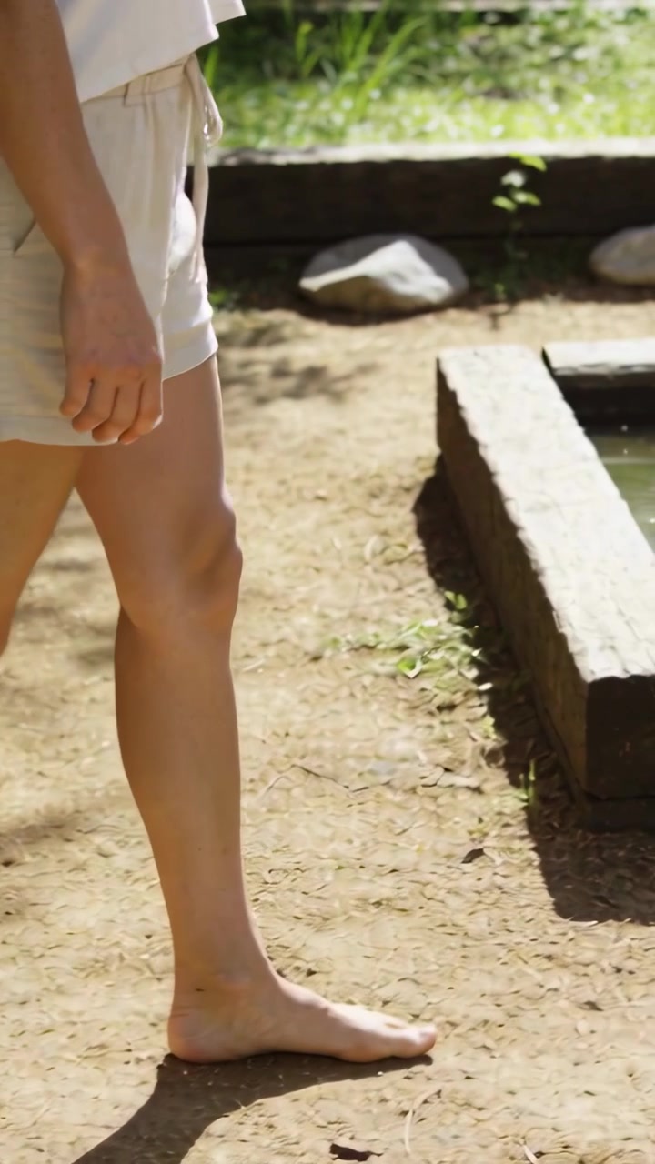 Video verticale: Donna a piedi nudi in pantaloncini chiari che cammina lungo un sentiero sterrato, spazio per il testo.
