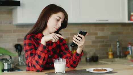 a young woman uses a smartphone he is sitting in his kitchen standing next to a glass of milk health