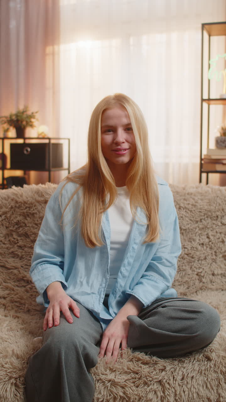 Young woman waving hello at home bright smile sofa joy relaxed mood friendly open greeting vibe