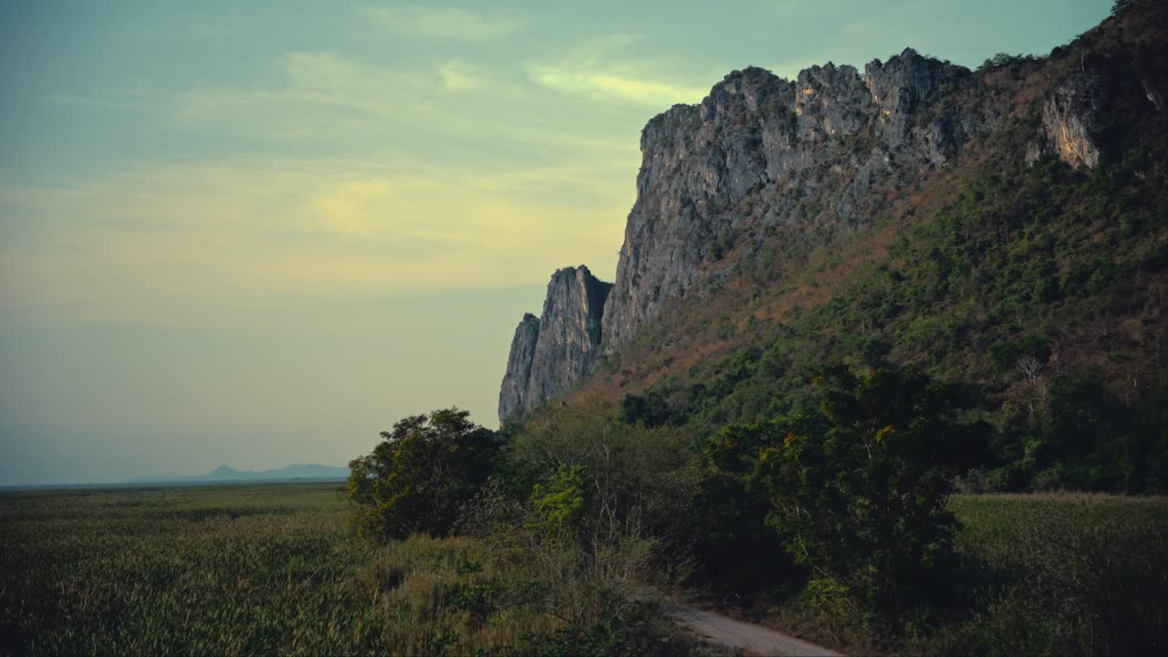 Limestone hills next to a marsh with a road in between in a national park in Thailand