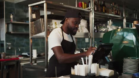 stylish black person in a cap - an employee of the doner market takes an order and works on an electronic guy in a cafe