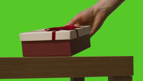 close up of man putting down gift wrapped present onto table shot against green screen 1