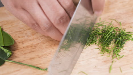 fine chopping up kaffir lime leaves with a knife on a wooden board, finely chopped kaffir lime leaves, thai food ingredients