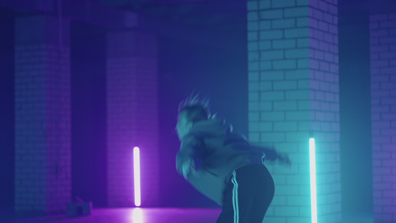 A steel woman dances hip-hop freestyle in a modern style in a hall with neon light in purple blue colors. Female Professional Hip Hop Dancer