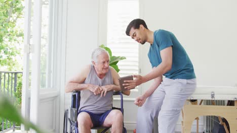 Male-fitness-coach-discussing-with-disabled-senior-man-on-wheelchair-in-health-club