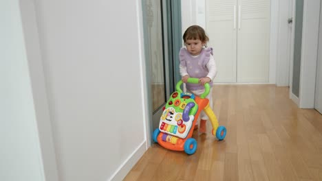 cute baby learning tow to walk with the help of sit-to-stand walker toy at a home corridor