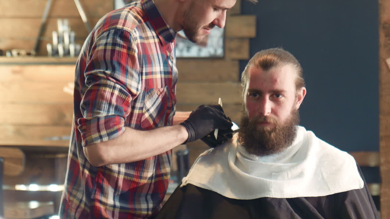 Barber trimming beard of customer in barber shop
