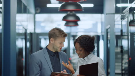 Multiracial-couple-scrolling-tablet-in-corridor.-Couple-talking-about-project