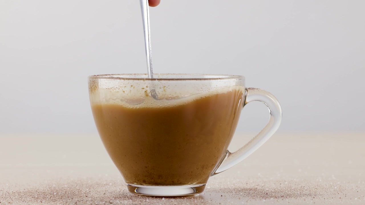 Primo piano di un cucchiaio di metallo che mescola caffè caldo in una tazza di vetro trasparente su un tavolo