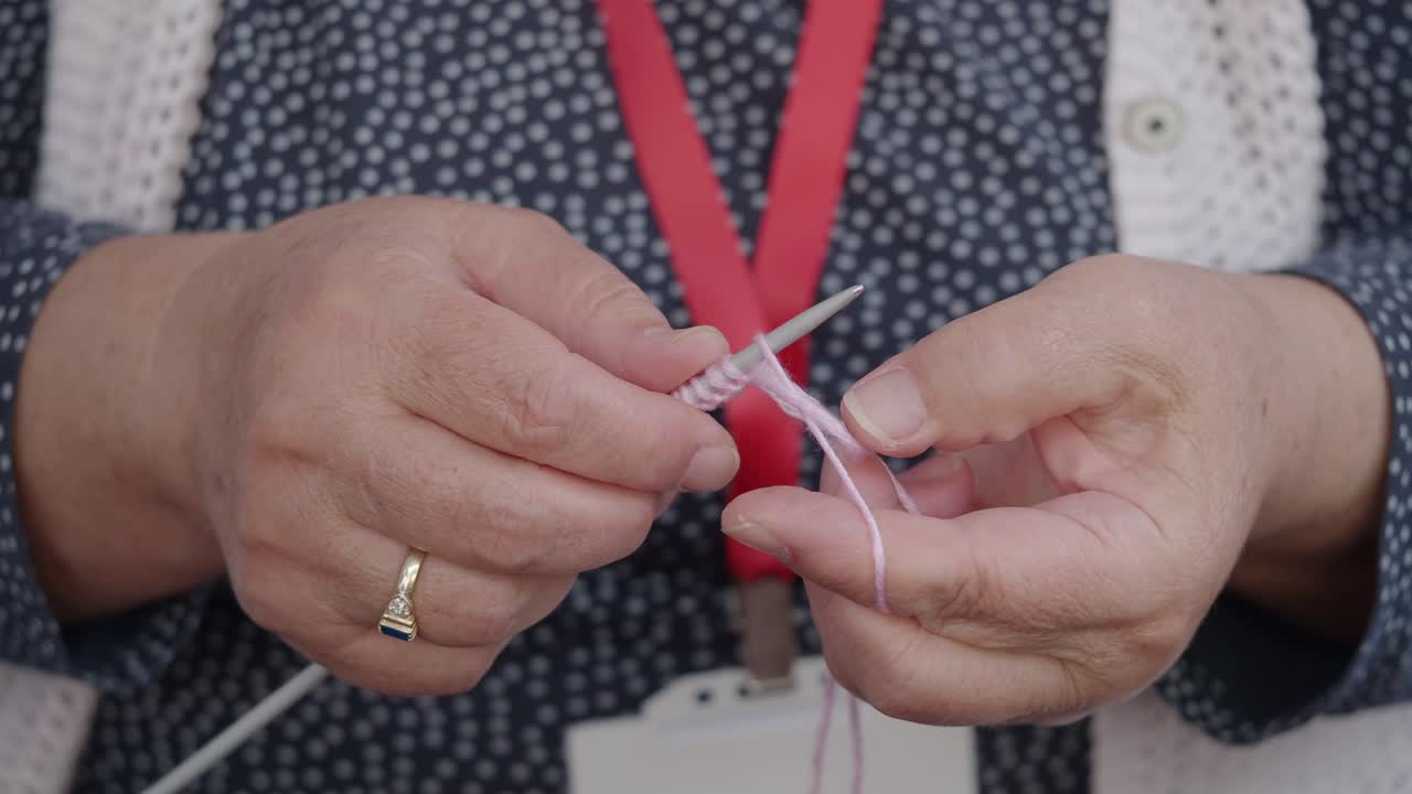 Primo piano di mani che lavorano a maglia con filato rosa
