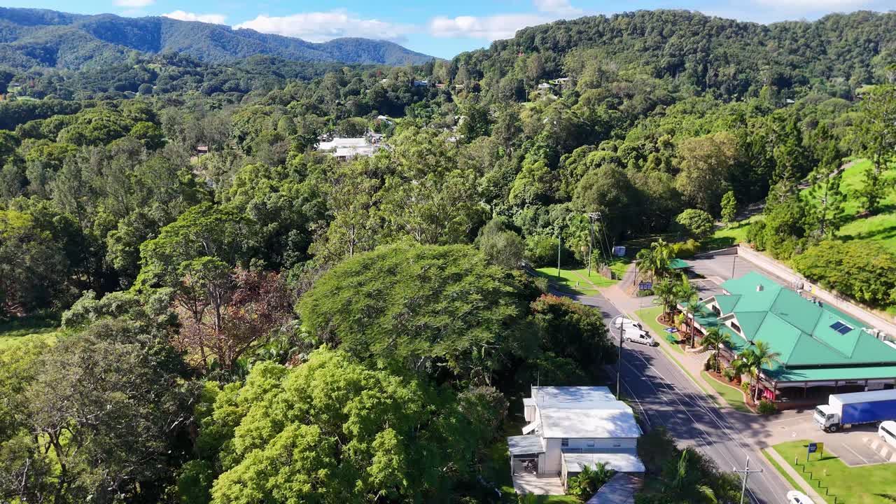 Drone footage captures lush greenery and a quaint town in Uki, NSW, under bright daylight, showcasing natural beauty and serene environment