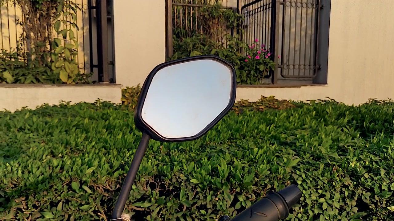 Primo piano del manubrio e dello specchietto retrovisore di una moto parcheggiata accanto al verde residenziale. Ideale per immagini di stile di vita urbano, temi di pendolarismo e contenuti sul trasporto quotidiano