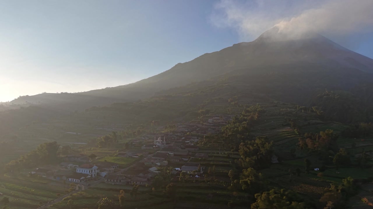 Splendida campagna sotto il Monte Merapi con campi verdi, case di villaggio e un vulcano attivo al tramonto. Filmato ideale per viaggi, natura e paesaggi.