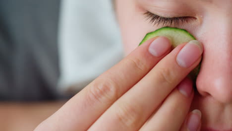 close-up side view of woman placing cucumber slice over her eye for relaxation, emphasizes soothing self-care routine with cucumber slice applied gently to her skin for cooling