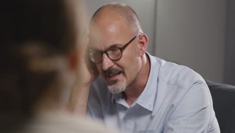 mature man sitting on sofa talking with female counsellor about general or mental health issue 21