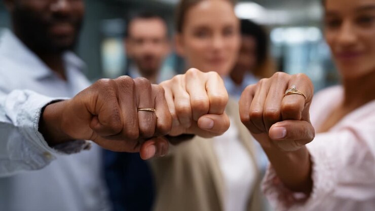 Un grupo diverso de personas que celebran la unidad y el espíritu de equipo en un entorno de oficina chocando los puños, enfatizando la colaboración y la camaradería entre compañeros.